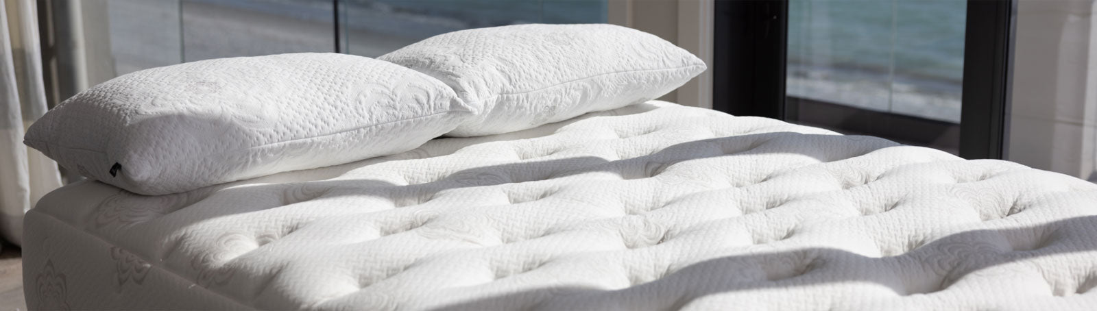 Close-up of the PranaSleep Dharma mattress featuring a deeply tufted quilted surface and matching pillows in a sunlit bedroom setting, highlighting luxurious craftsmanship and elevated comfort.