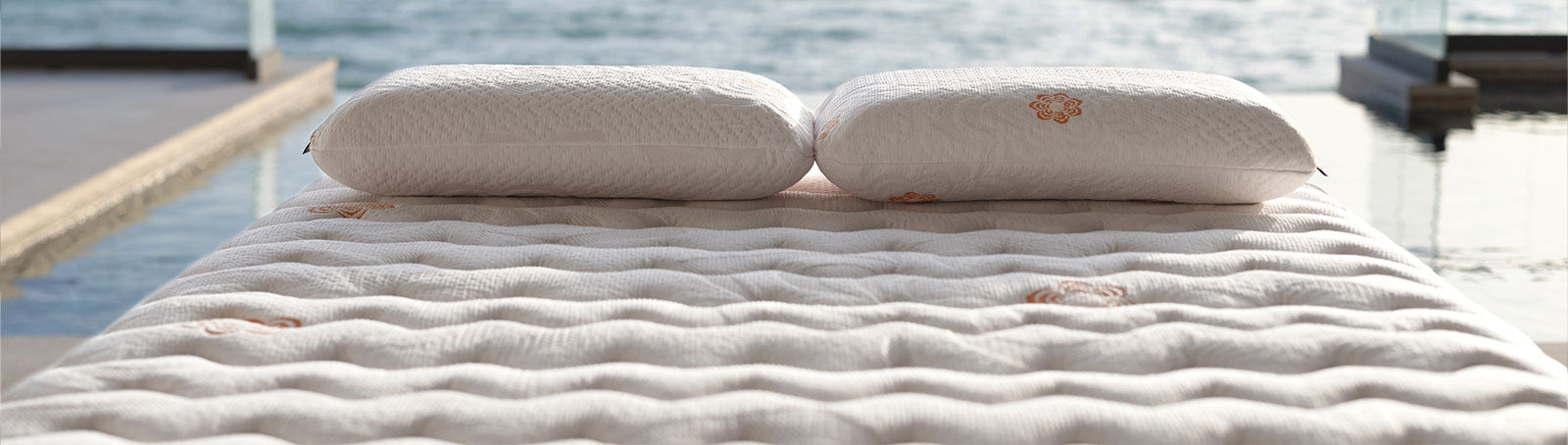 A close-up of Karma mattress with two matching white pillows, set outdoors near water.