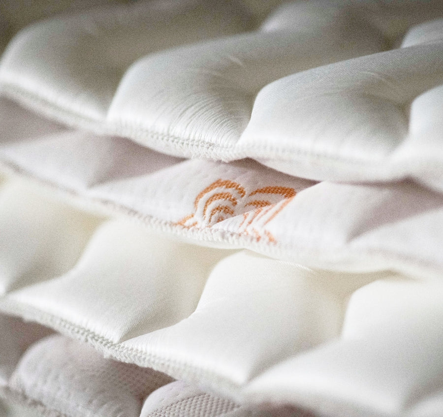 Close-up detail of plush, hand-tufted PranaSleep Karma mattress surface featuring soft, pillowy quilting and an embroidered PranaSleep logo accent, highlighting luxurious comfort and meticulous craftsmanship.